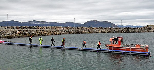 6 people walking on a pier over to a floating conveyor belt.